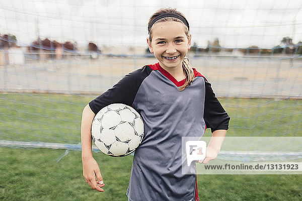Portrait of smiling girl holding soccer ball while standing on field