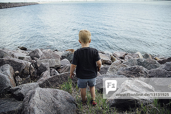Rear view of boy standing at rocky beach