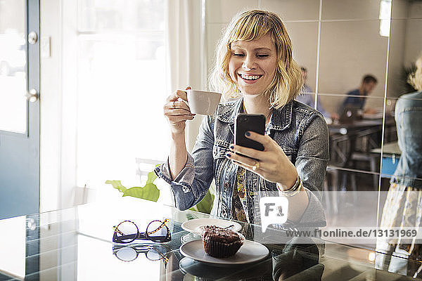 Glückliche Frau  die ein Smartphone benutzt  während sie im Cafe steht