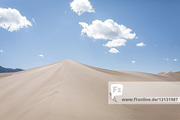 Hochwinkelaufnahme einer Frau die am sonnigen Tag auf eine Sanddüne im Nationalpark klettert