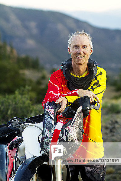 Portrait of man holding helmet while standing by dirt bike