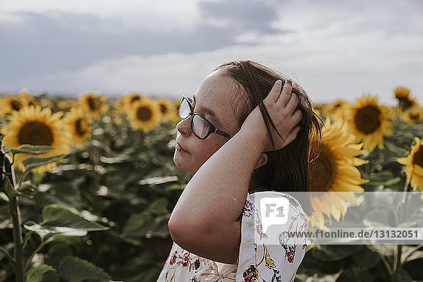 Nahaufnahme eines Mädchens mit Hand im Haar  das im Sonnenblumenfeld gegen den Himmel steht