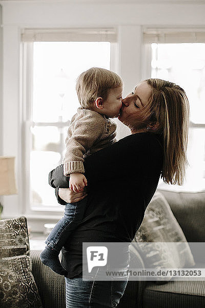 Mutter küsst Sohn  während sie ihn zu Hause im Wohnzimmer trägt