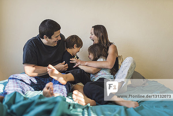 Cheerful parents playing with children on bed at home