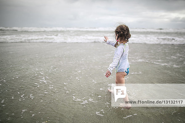 Full length of girl gesturing while walking in sea on shore