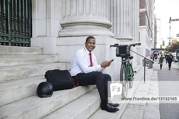 Portrait of happy businessman using mobile phone while sitting on steps
