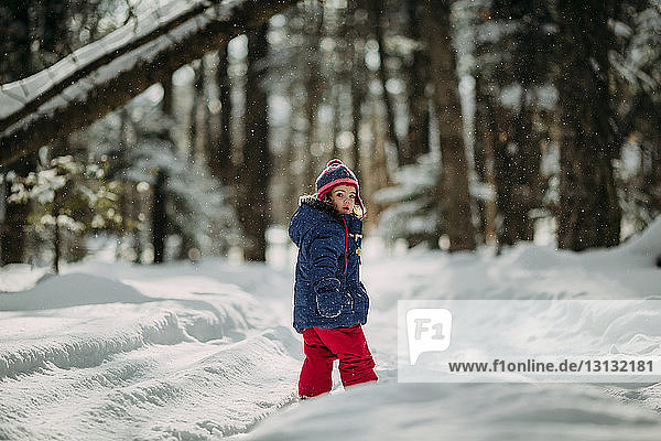 Portrait of girl standing on snow covered field in forest