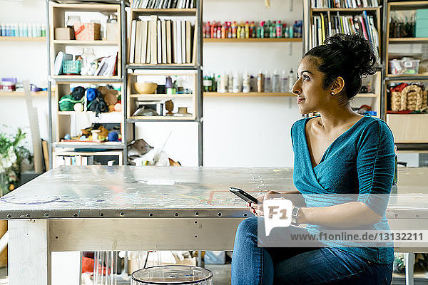 Nachdenkliche Geschäftsfrau benutzt Smartphone  während sie im Büro sitzt