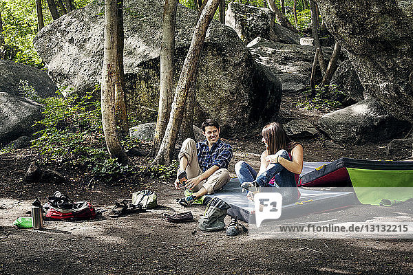 Happy couple relaxing on field against rocks at forest