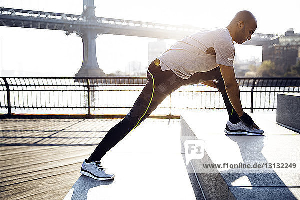 Seitenansicht eines männlichen Athleten beim Training auf der Promenade mit der Manhattan Bridge im Hintergrund