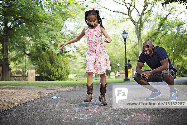 Vater und Tochter spielen Himmel und Hölle auf der Straße im Park