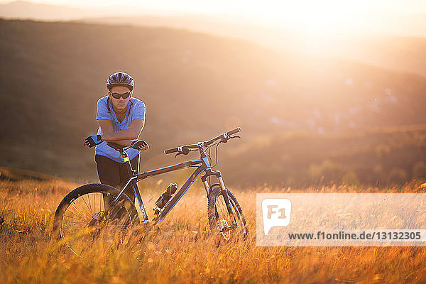 Porträt eines männlichen Athleten  der bei Sonnenuntergang mit dem Fahrrad auf dem Feld steht