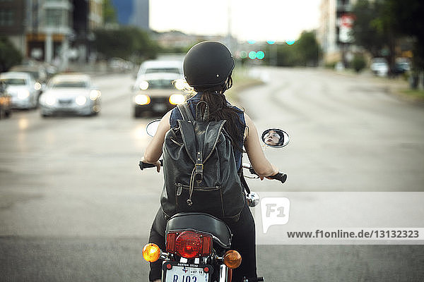 Rückansicht einer Frau mit Rucksack auf einem Motorrad auf der Straße