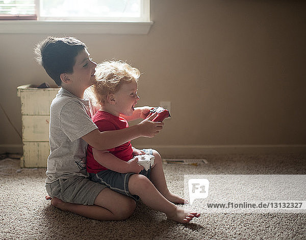 Seitenansicht von Brüdern  die zu Hause auf dem Teppich sitzend Videospiele spielen