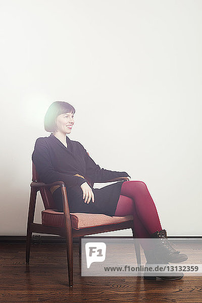 Glückliche Frau sitzt auf Stuhl an weißer Wand