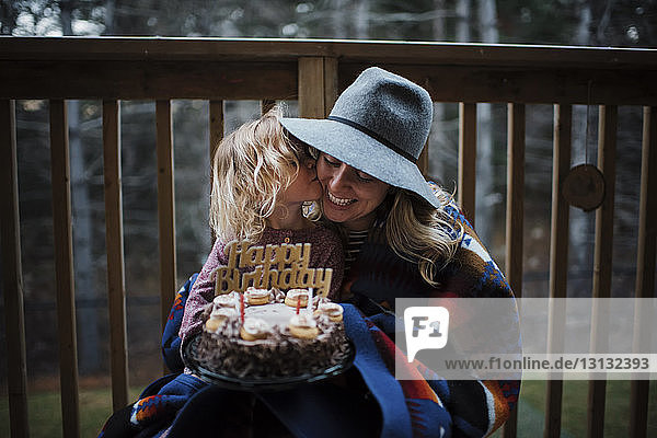 Tochter küsst Mutter  während sie Geburtstagskuchen auf dem Balkon hält