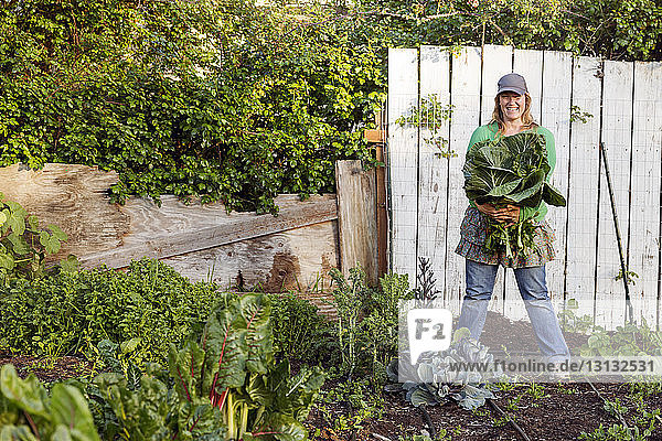 Porträt einer Bäuerin  die lächelnd frisch geerntetes Gemüse auf dem Bauernhof hält