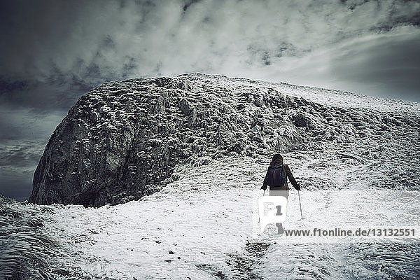Rear view of female hiker walking on snow covered mountain against cloudy sky