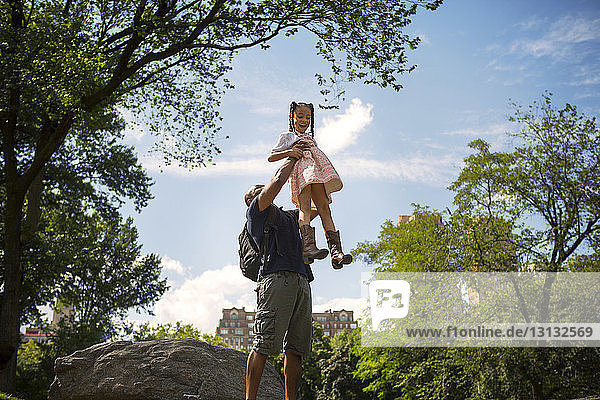 Low angle view of father carrying daughter against sky
