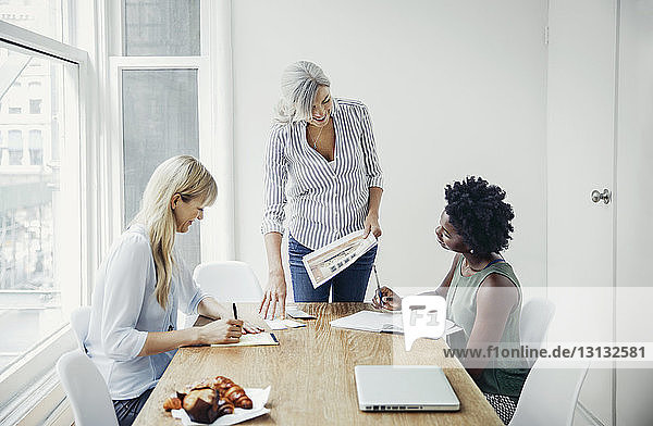 Mature businesswoman discussing over documents with female colleagues in board room