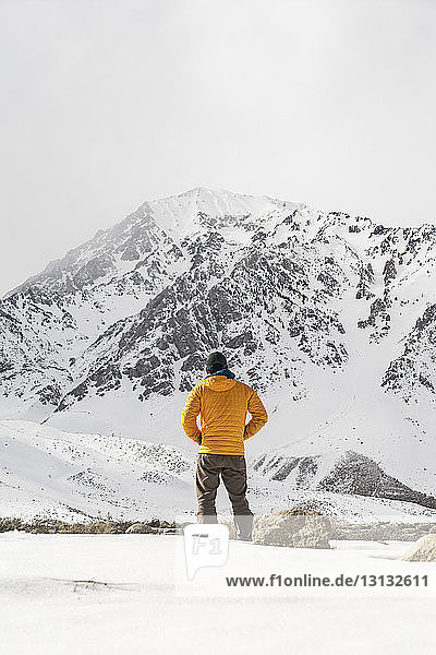 Rückansicht eines auf einem schneebedeckten Feld stehenden Mannes gegen den Himmel