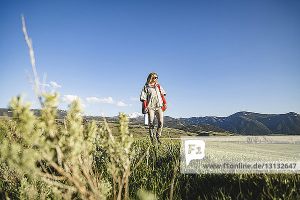 Female hiker walking on field against sky