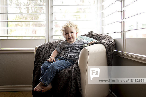 Porträt eines süßen Jungen  der zu Hause auf einem Stuhl vor dem Fenster sitzt