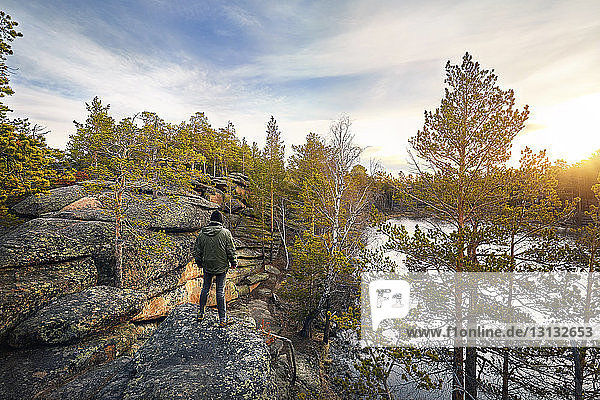 Rückansicht eines auf einer Felsformation stehenden Mannes vor bewölktem Himmel im Wald