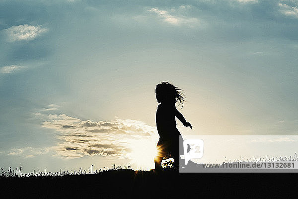 Silhouette girl walking on field against sky during sunset