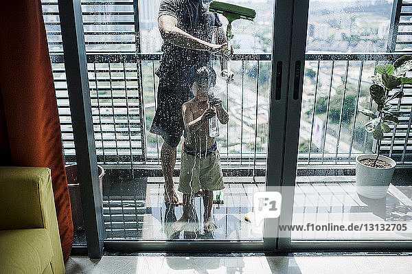 Niedrige Sektion eines Vaters mit Sohn beim Fensterputzen auf dem Balkon durch Glas gesehen