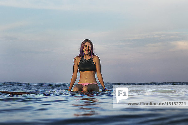 Glückliche Frau sitzt bei Sonnenuntergang auf einem Surfbrett im Meer