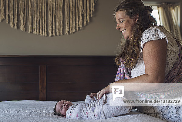Lächelnde Mutter wickelt neugeborene Tochter mit Decke auf Bett zu Hause