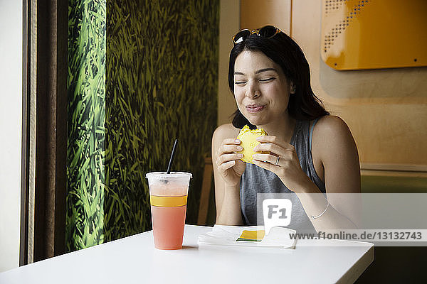 Glückliche Frau isst Makrone und trinkt Saft im Restaurant