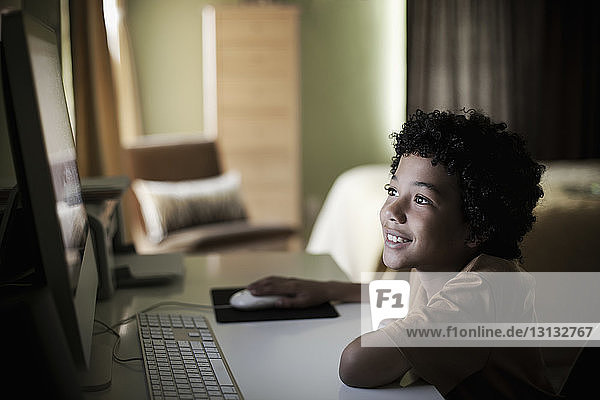 Lächelnder Junge  der zu Hause am Computer sitzt