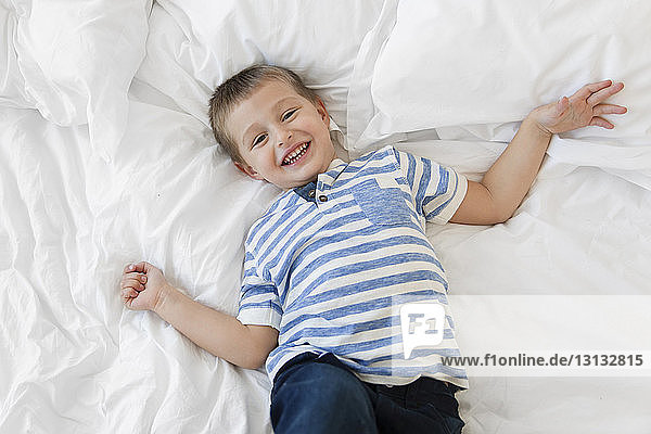 Hochwinkelporträt eines fröhlichen Jungen  der zu Hause auf dem Bett liegt