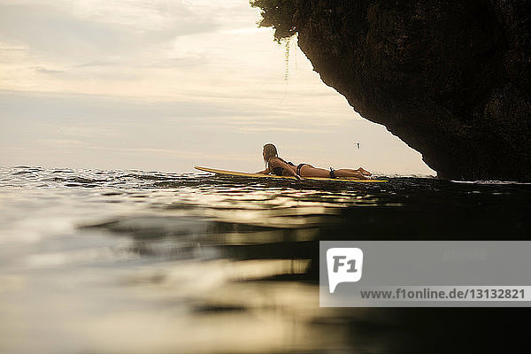 Seitenansicht einer Frau  die bei Sonnenuntergang im Meer surft