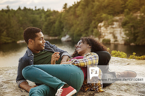 Glückliches Paar unterhält sich beim Entspannen auf einem Felsen am Seeufer