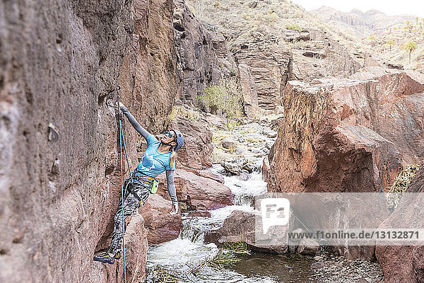 Weibliche Wanderin mit Seil beim Klettern auf Felsformation am Fluss