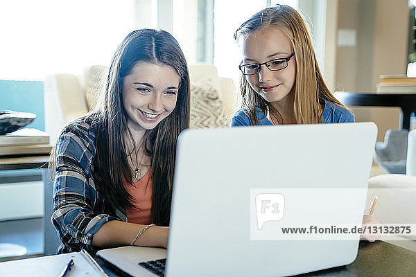Schwestern benutzen Laptop-Computer  während sie zu Hause Hausaufgaben machen