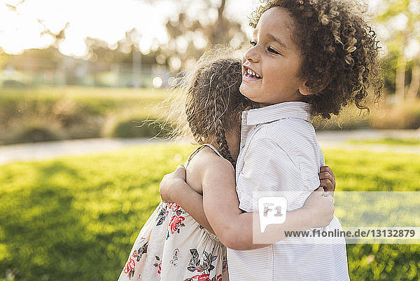 Side view of happy siblings embracing at park