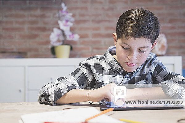 Boy sticking out tongue while drawing on tablet computer at table