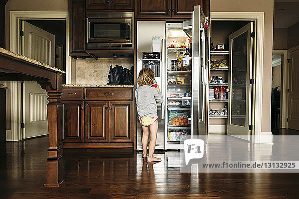 Junge trinkt  während er in der Küche zu Hause am Kühlschrank steht