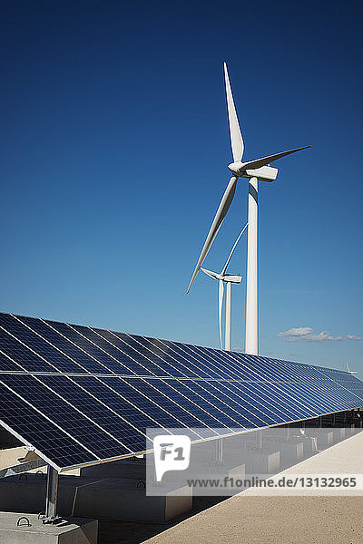 Sonnenkollektoren auf Fabrik bei Windmühlen gegen blauen Himmel