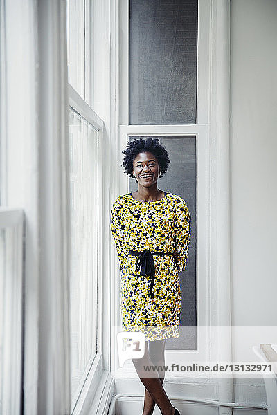 Porträt einer glücklichen Geschäftsfrau  die in einem kreativen Büro am Fenster steht
