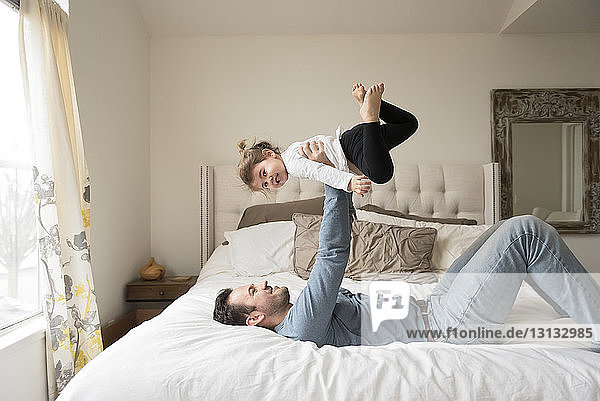 Playful father lifting daughter while on bed at home