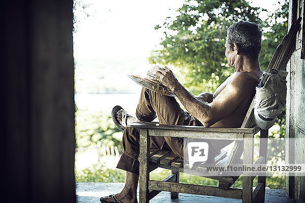 Seitenansicht eines Mannes  der sich auf einem Stuhl auf der Veranda entspannt