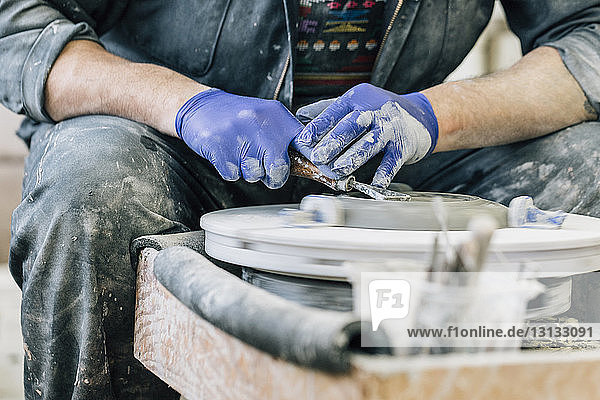 Midsection of craftsman using pottery wheel while working in art studio