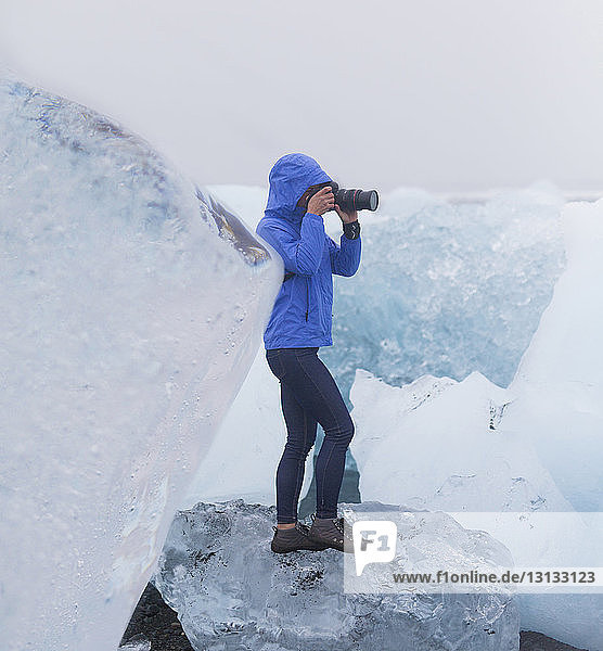 Touristin in voller Länge beim Fotografieren mit der Kamera  während sie auf dem Gletscher steht