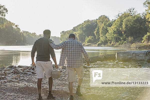 Rear view of male friends with fishing rods walking on rocks by lake