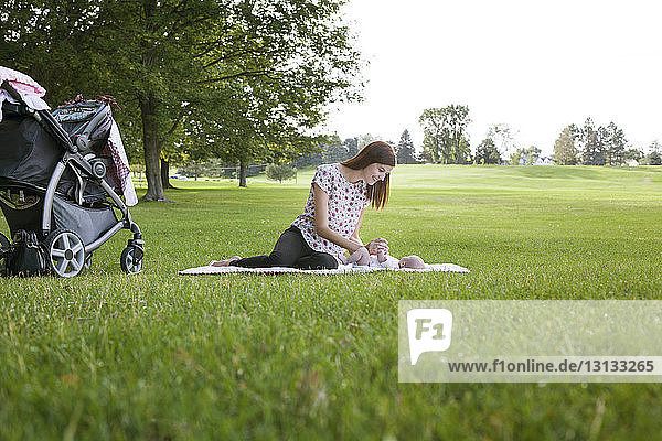 Mutter spielt mit dem Baby  während sie sich auf dem Grasfeld im Park ausruht